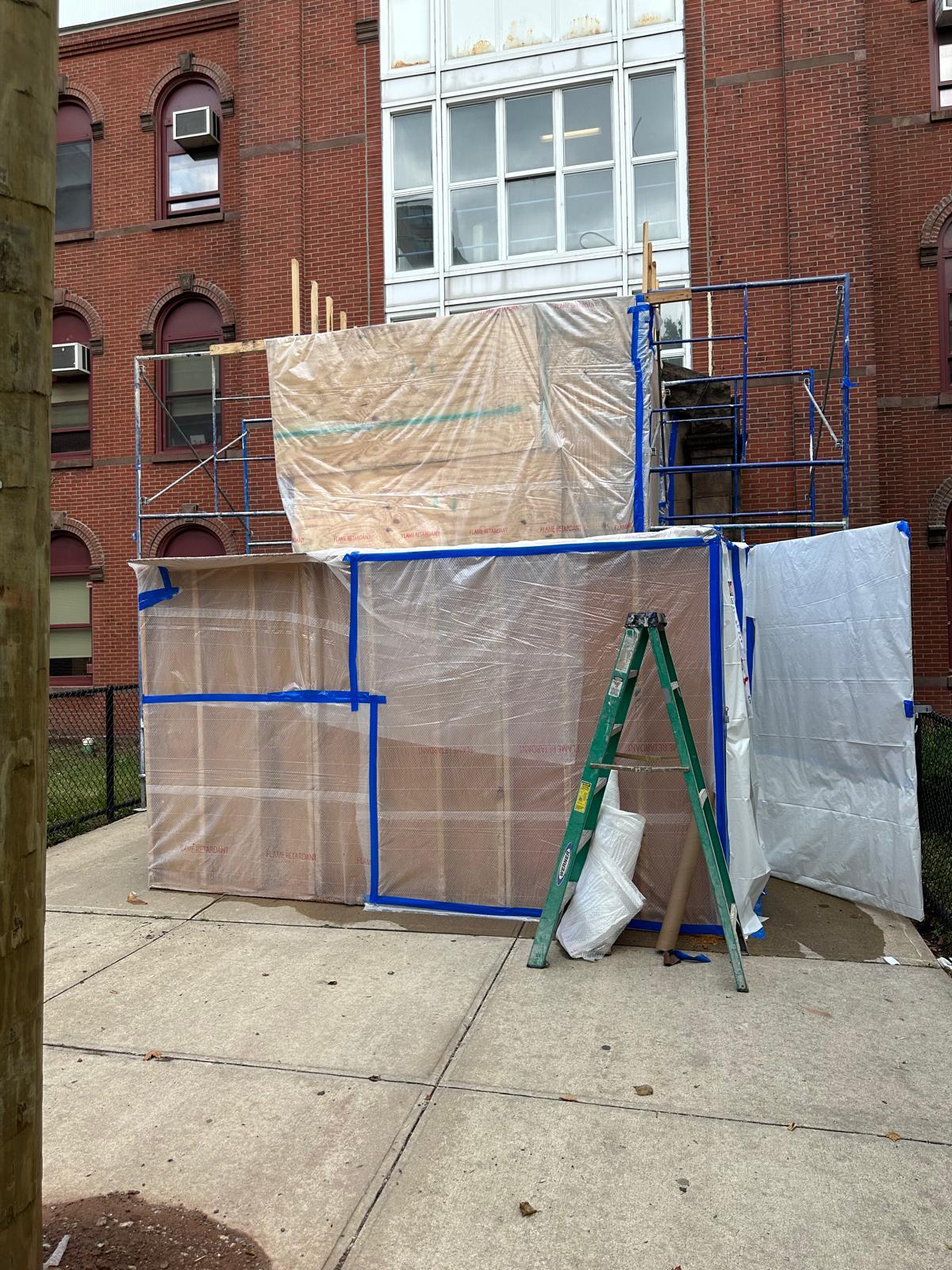 Scaffold-mounted containment tent on a brick institutional building sidewalk