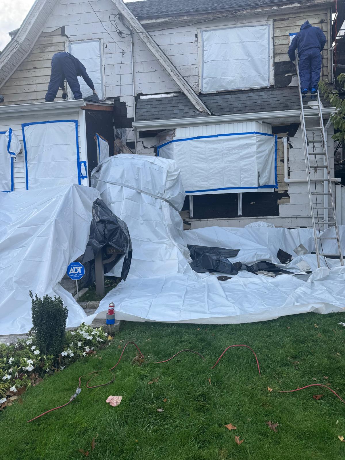 ABBN crew in protective suits removing asbestos siding from a two-story home
